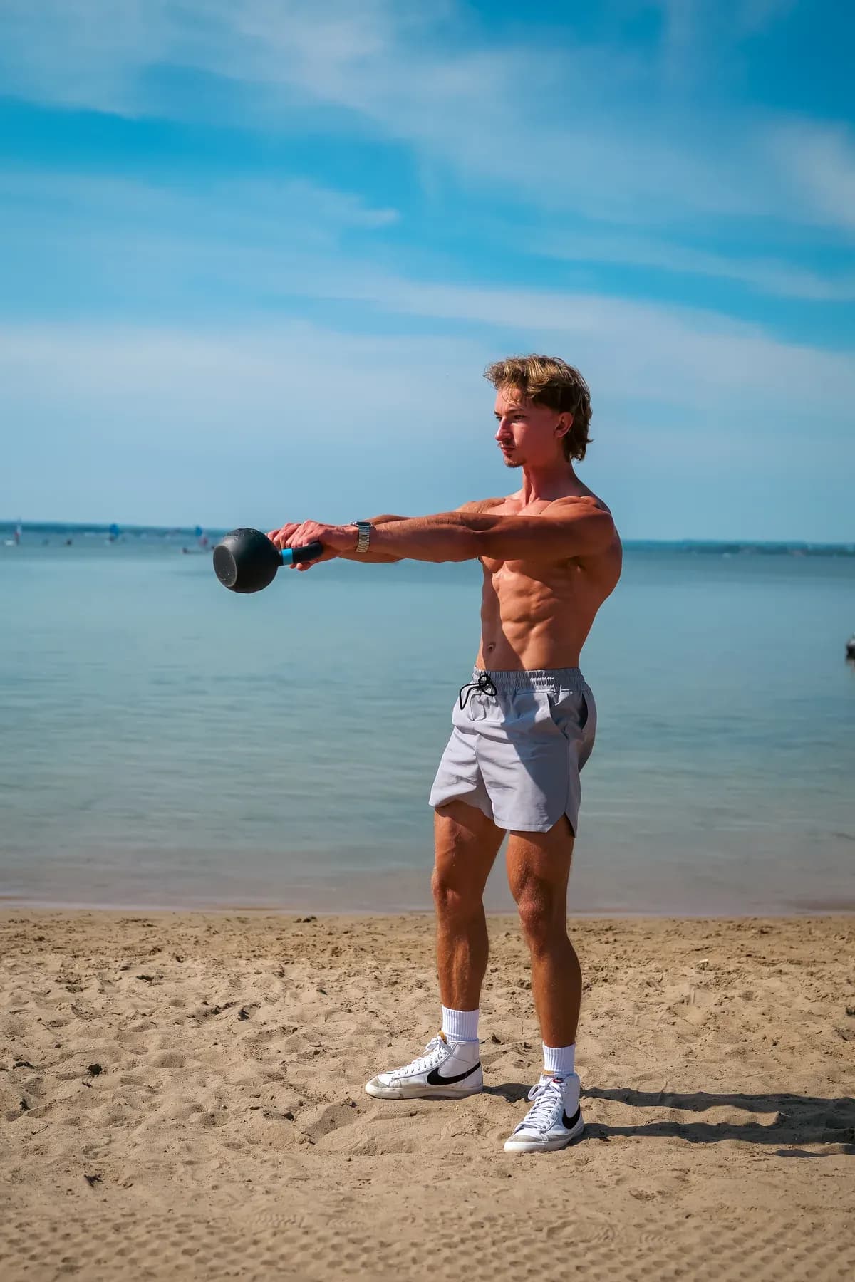 Kacper Dutkiewicz wykonuje wymach kettlebellem na plaży